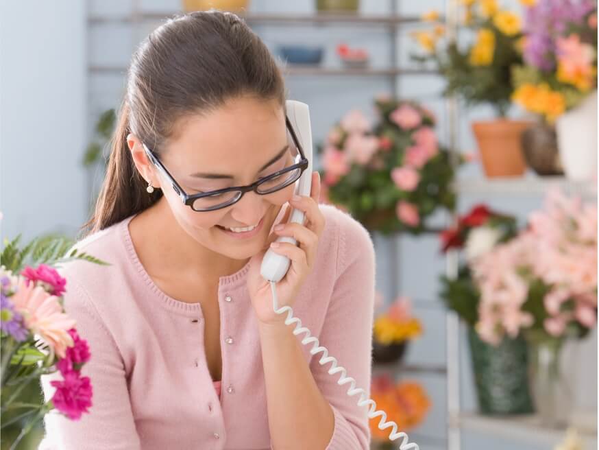 Woman in in florist shop talking on a desk phone.